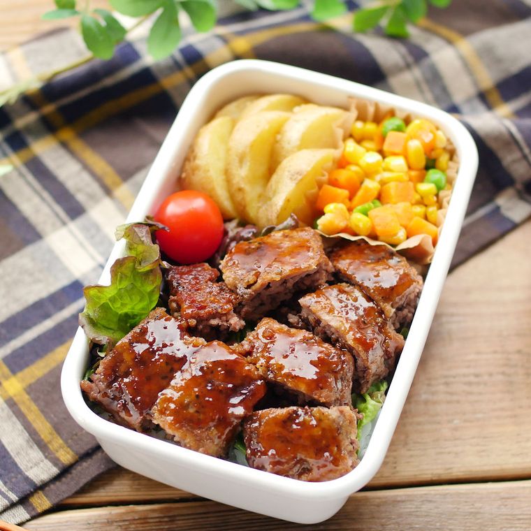 白い弁当箱に入っているサイコロステーキとガーリックポテトなど