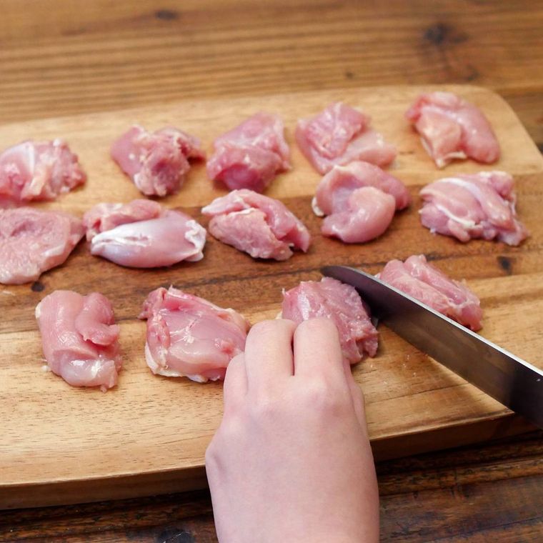 まな板の上で鶏もも肉をぶつ切りしている様子