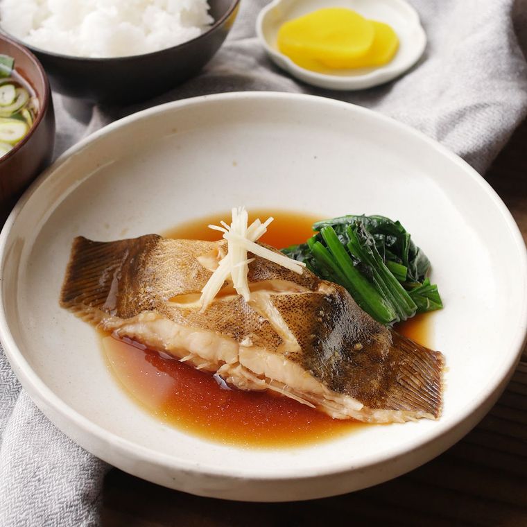 白い皿に盛り付けられたかれいの煮付けと青菜のつけ合わせ