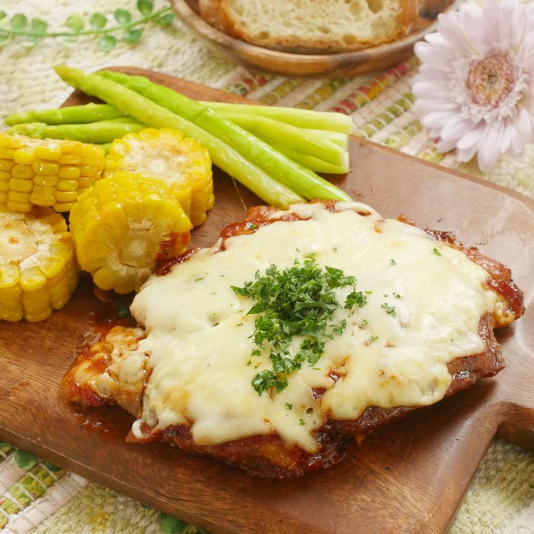 ウッドプレートに盛り付けたチキンステーキとアスパラガス、とうもろこし