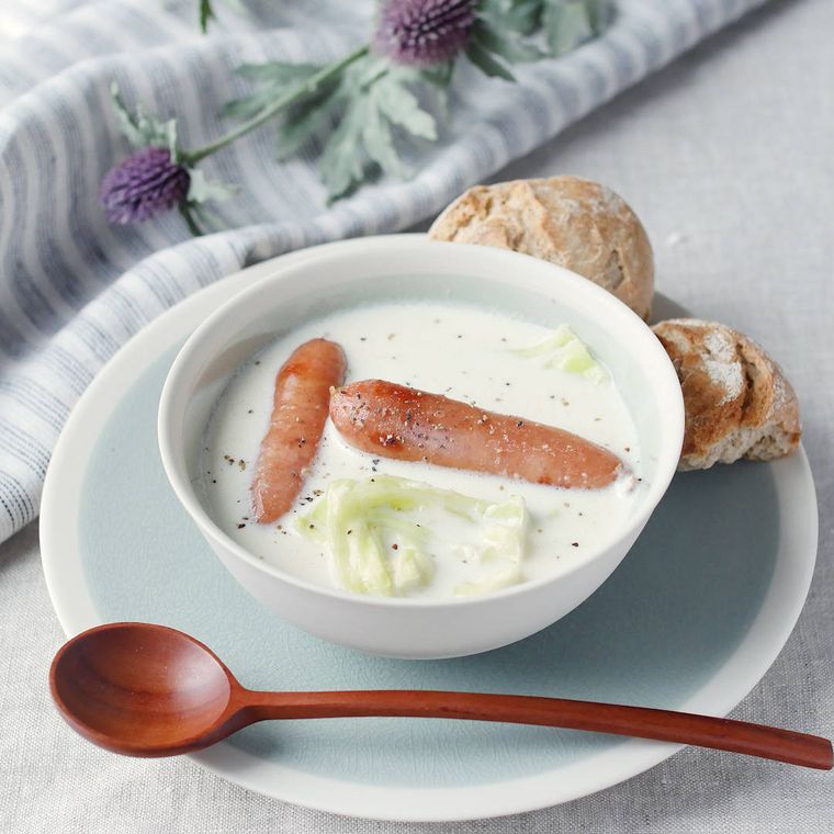 水色のソーサーの上にある白いカップに入っているウインナーのミルクスープ