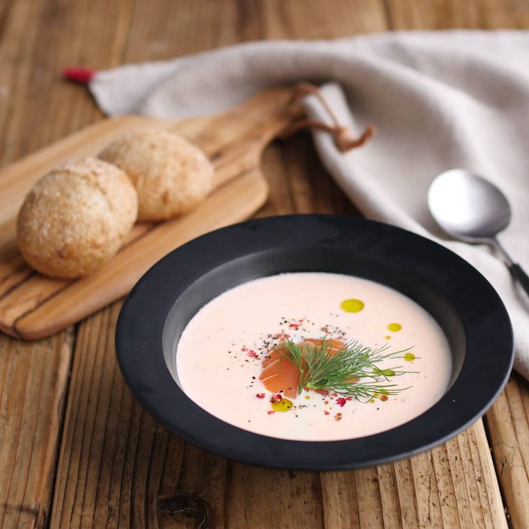 黒いスープ皿に盛られているスモークサーモンのクリームスープ