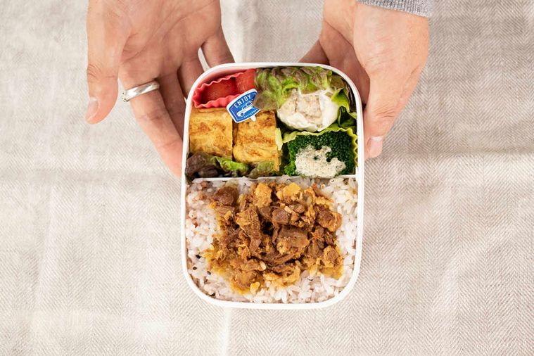 角煮が乗ったご飯が入った、プラスチックのお弁当箱をもっている