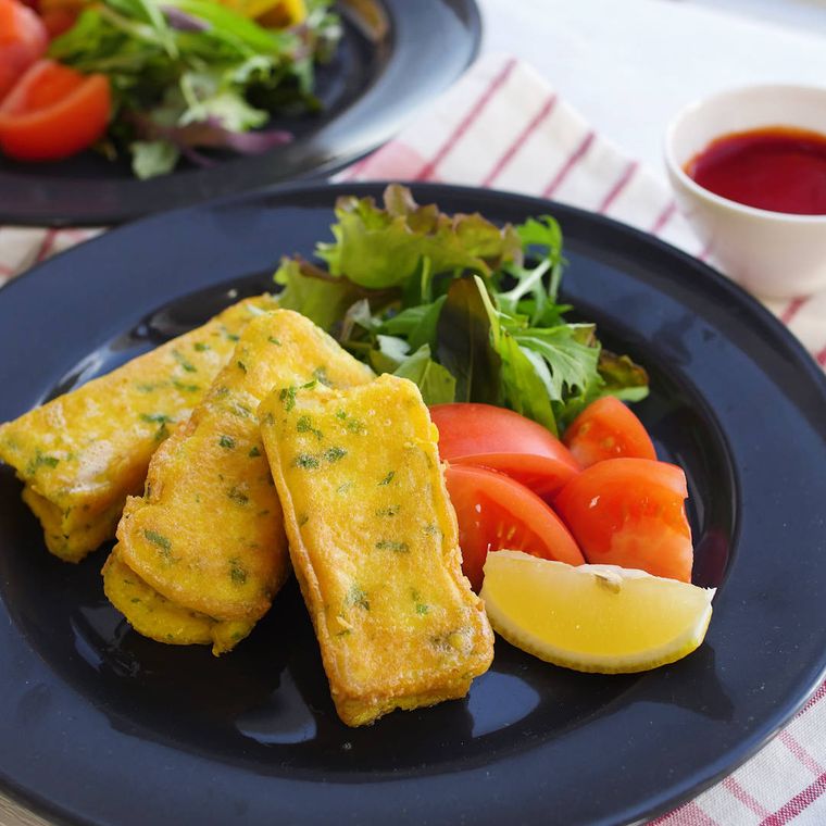 黒い皿に盛り付けられた厚揚げのピカタ、トマトなどのつけ合わせ