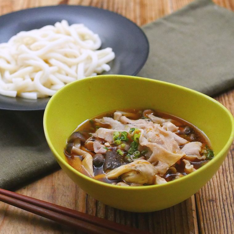 黒いお皿に盛られたうどんと、黄緑色の器に盛られた豚肉ときのこのつけ汁