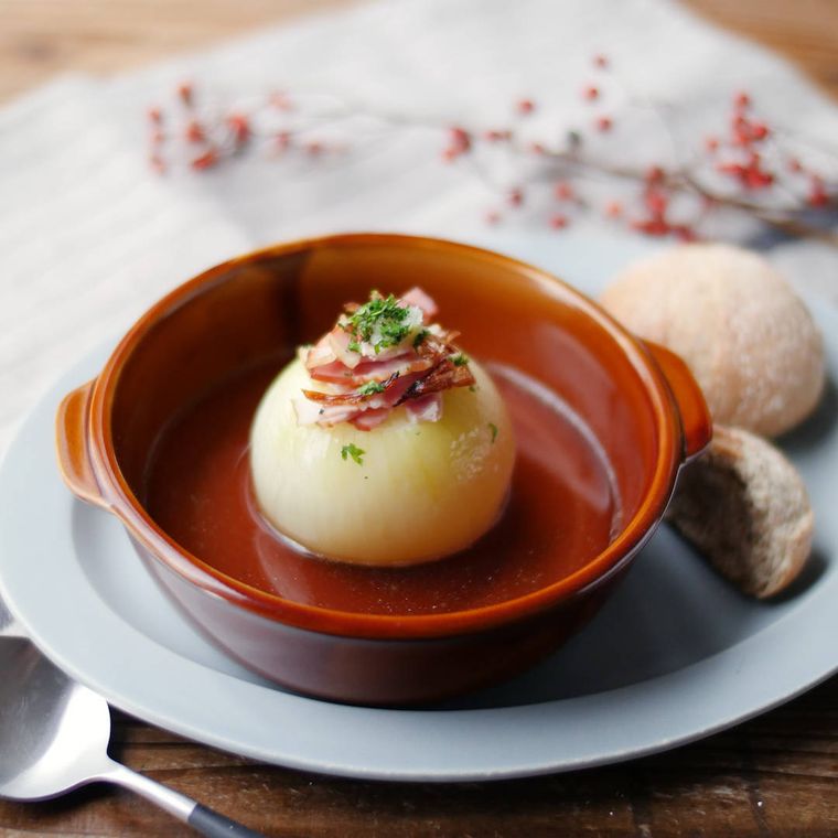 手付きの茶色のグラタン皿に入ったまるごと玉ねぎのコンソメスープ