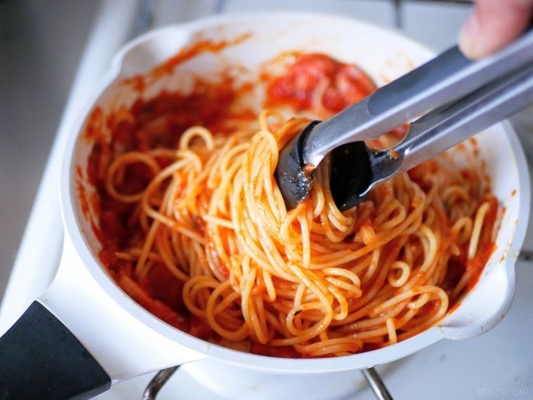白いフライパンに入ったトマトパスタをトングでつかんでいる