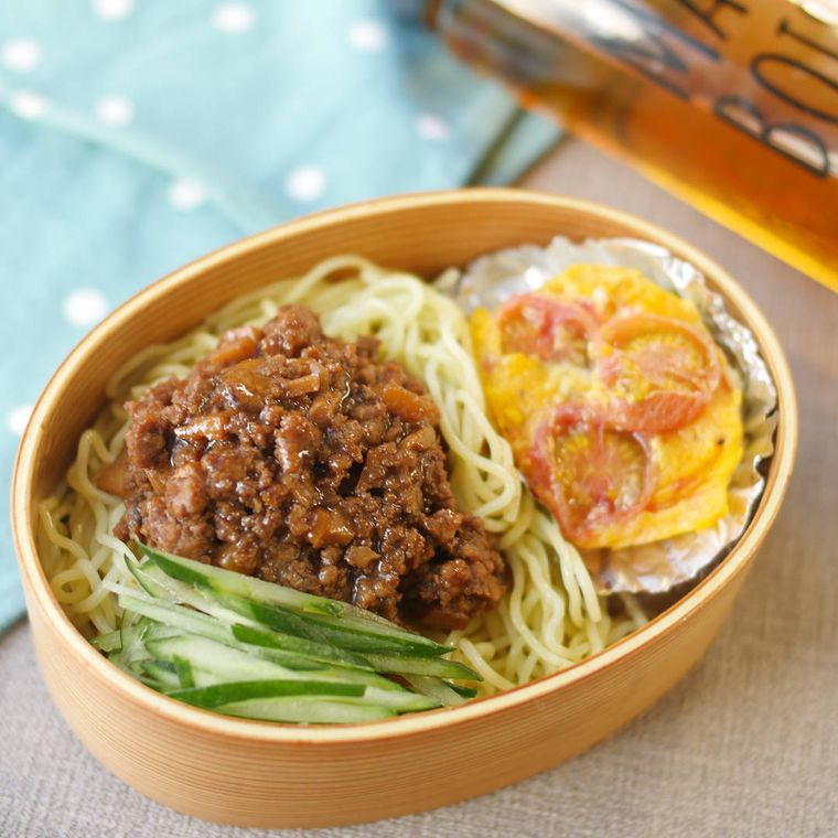 木の弁当箱の中に入ったジャージャー麺とトマトと卵の炒め物