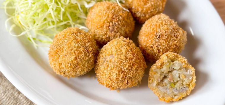 白い皿に盛りつけられた里芋と豚ひき肉のチーズコロッケ