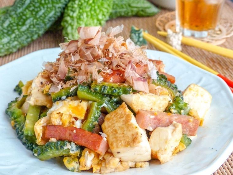 ゴーヤチャンプルーを盛ったお皿とゴーヤがある食卓