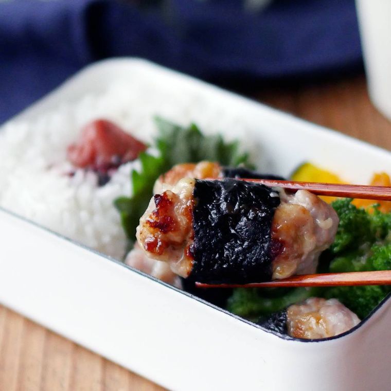 弁当箱に入った豚肉のチーズ海苔巻きを箸で持っている様子