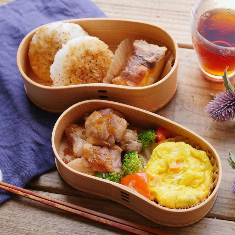 曲げわっぱの弁当箱におかずやおにぎりが入っている