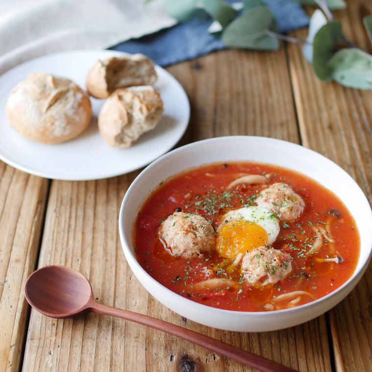 スープ皿に盛られた鶏だんごと半熟卵の塩麹トマトスープと丸パンがのったプレート