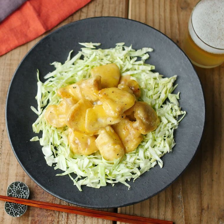 千切りキャベツを敷いた黒い皿に盛られた、鶏むね肉のエビマヨ風