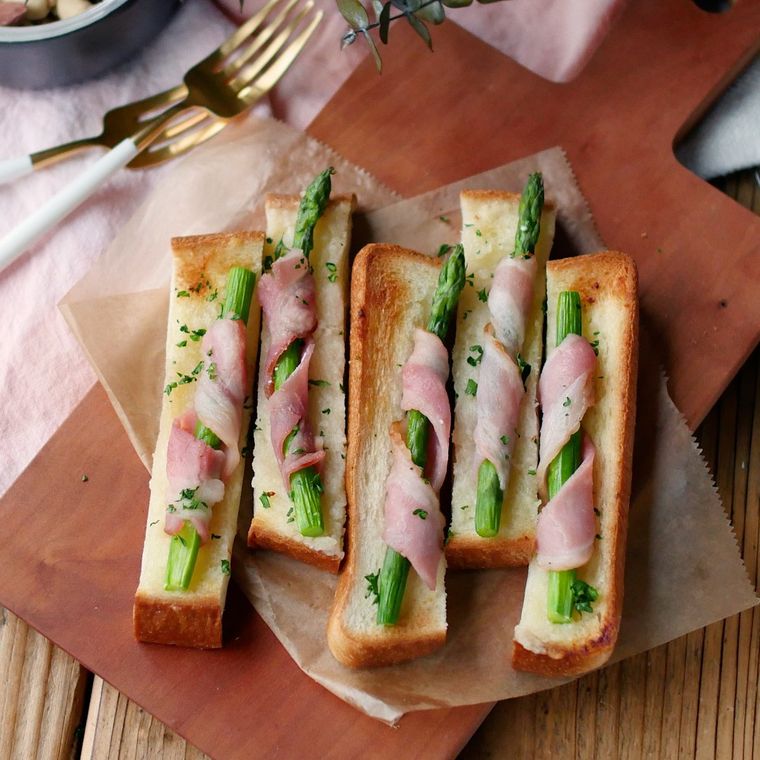 クッキングシートの上に並ぶアスパラベーコンのガーリックトースト