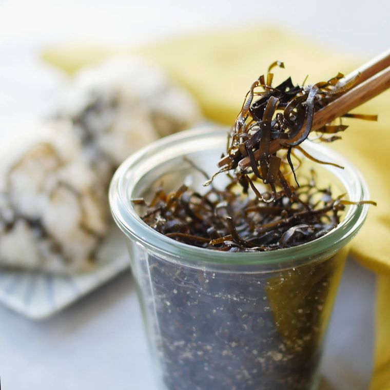 透明な容器に入った塩昆布を、箸で取り上げる様子