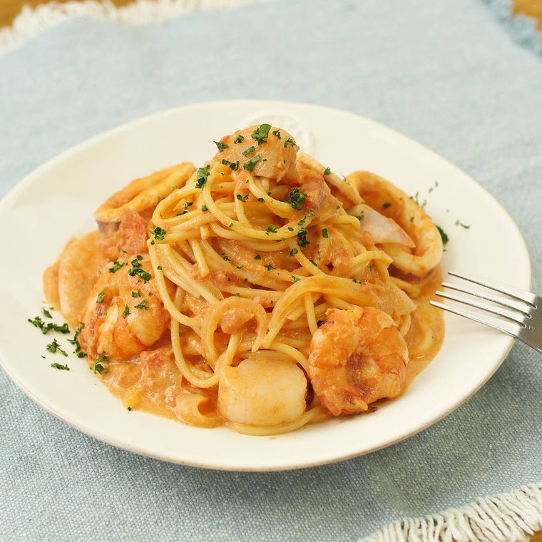 白い皿に盛りつけられたえびとほたて、いかのマトクリームパスタ