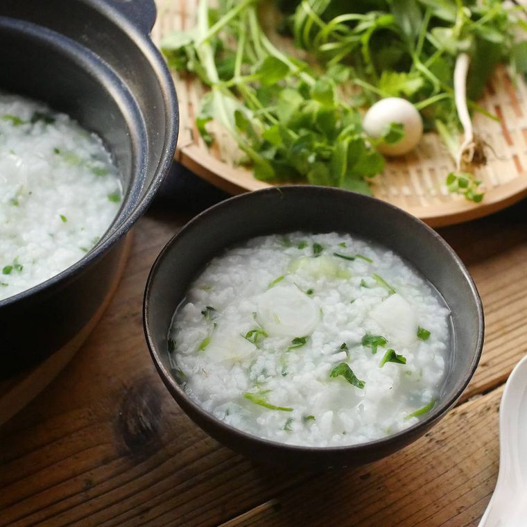 黒い器に盛られた七草粥と、竹ざるに入った七草