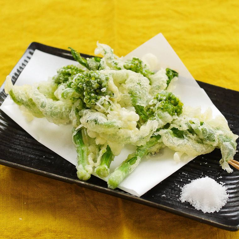菜の花の天ぷらが、塩をそえた黒い皿に盛り付けられている