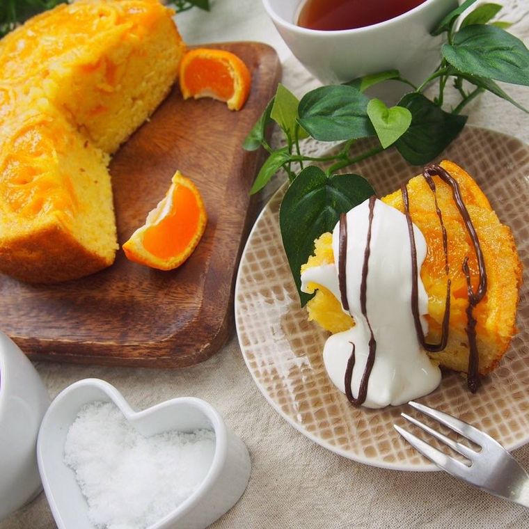 茶色いチェック柄の皿に盛り付け、クリームとチョコがかけられたはちみつみかんケーキ