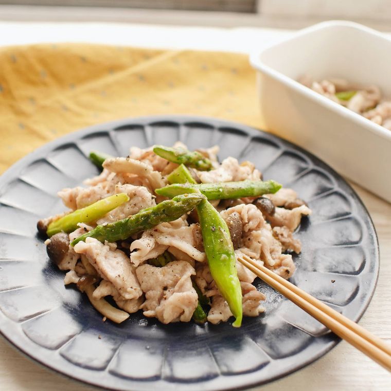 黒い丸いプレートに盛り付けられた豚肉とアスパラの黒こしょう炒め
