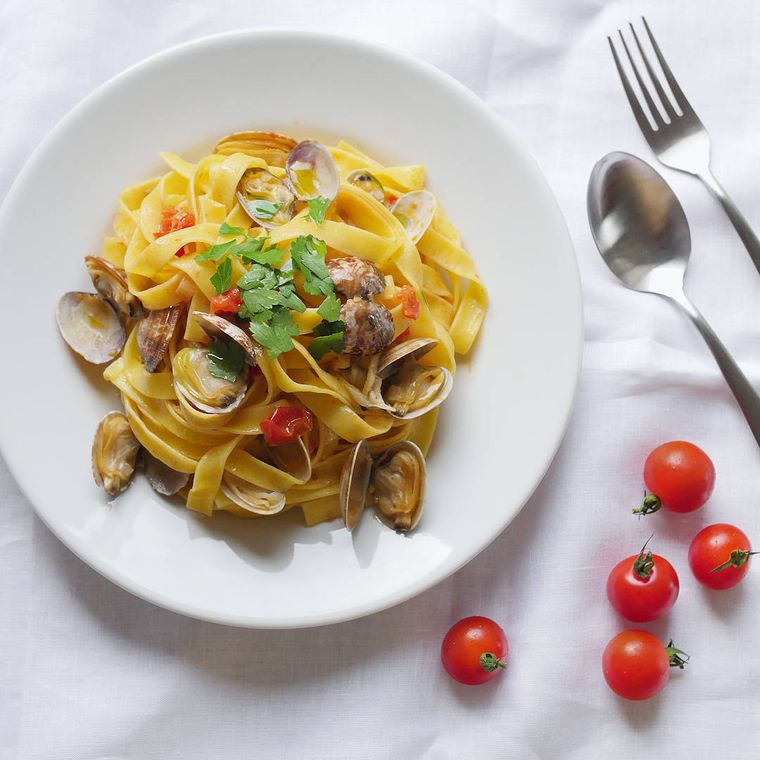 白い皿に盛り付けたボンゴレマキアート、ころがるミニトマト、カトラリー