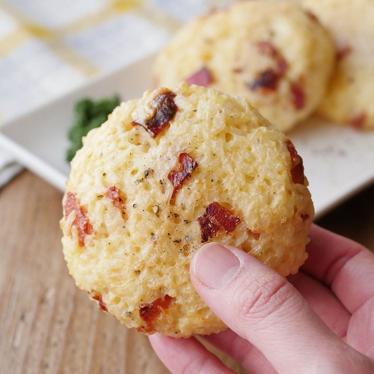 チーズでこんがり焼かれた丸いカルボナーラおにぎりを持っている