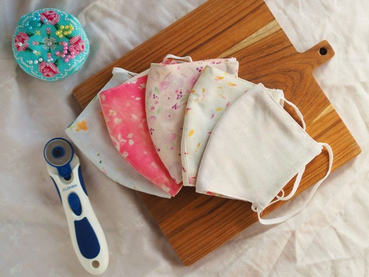 重ねて並べられたカラフルな手作りマスク5枚と針山、ロータリーカッター