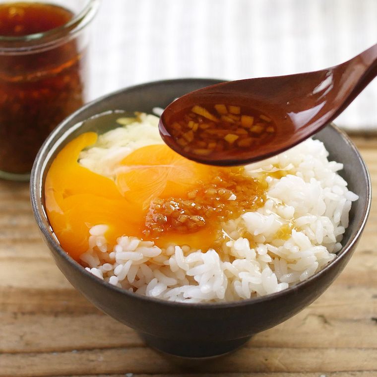 黒いお茶碗に盛り付けた卵かけご飯に、さっぱり生姜だれをスプーンでかけている様子