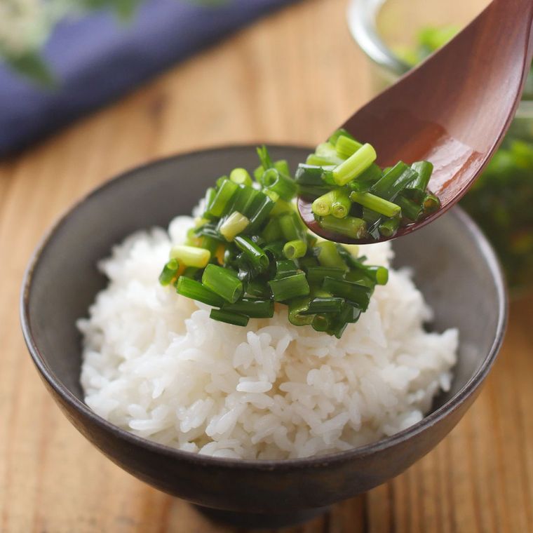 黒いお茶碗によそったご飯に、スプーンで小ねぎのごま油漬けをかけている様子