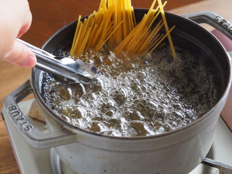 湯が沸騰した鍋にパスタを入れてトングでかき混ぜる様子