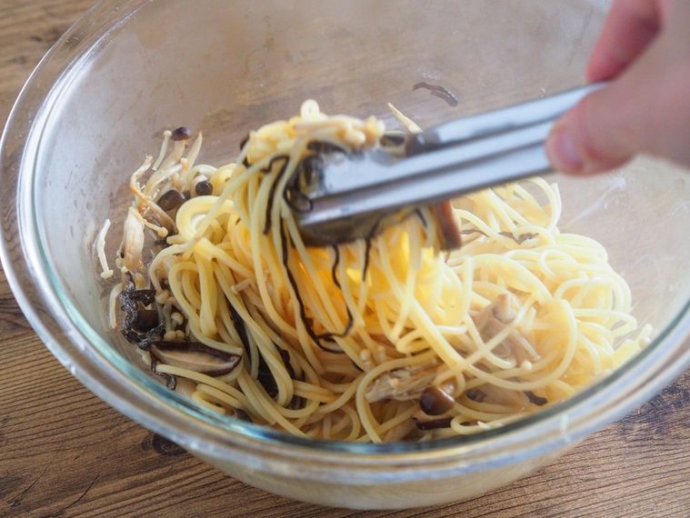 ボウルに入ったパスタときのこ、バター、塩昆布をトングで和える様子