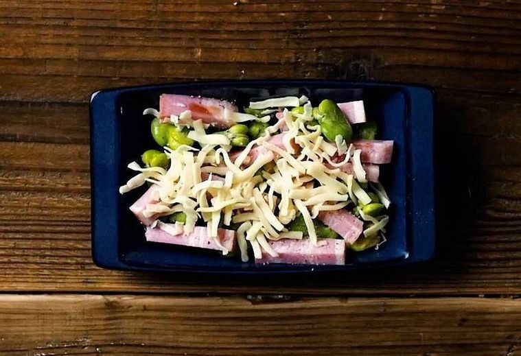 紺色の皿に入った焼く前のそら豆とベーコンのカリカリチーズ焼き