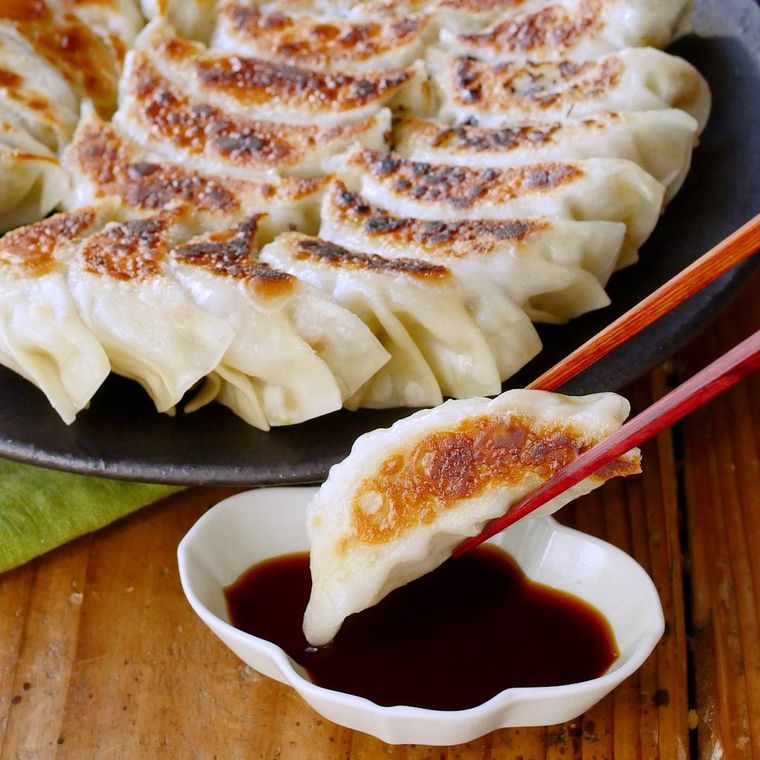 黒い皿に餃子が並び、箸で餃子をタレにつけている様子