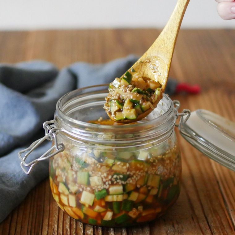 透明な保存瓶に入ったきゅうりのうま辛ダレ漬けを、木製のスプーンですくっている様子