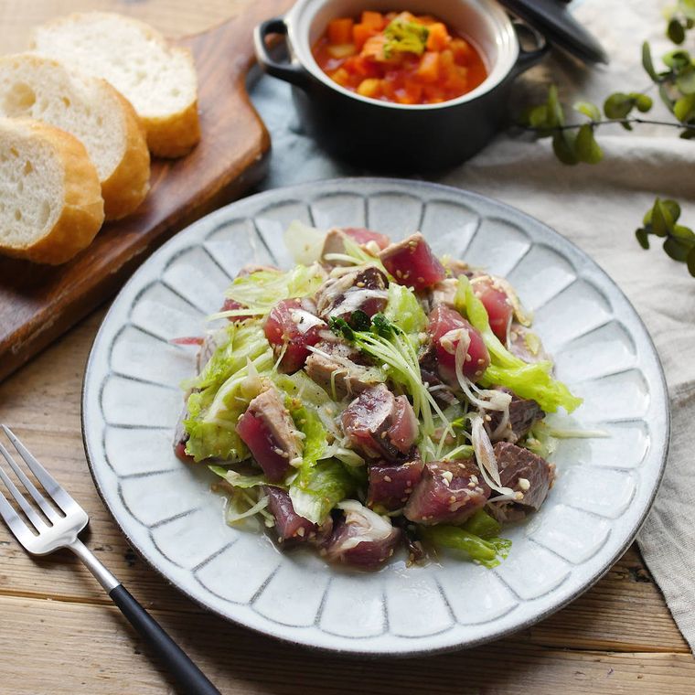 丸いお皿にねぎ塩かつおのたたきサラダが盛られている。奥にバゲットとミネストローネも置かれている