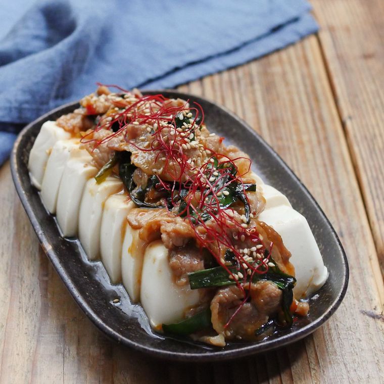 俵型の黒い皿に冷奴と、その上に豚肉とニラ炒めがのっている