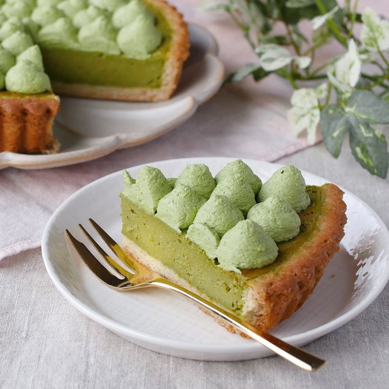 切り分けた抹茶のチーズタルトを盛り付けた白い丸皿に、金色のフォークが添えられている様子