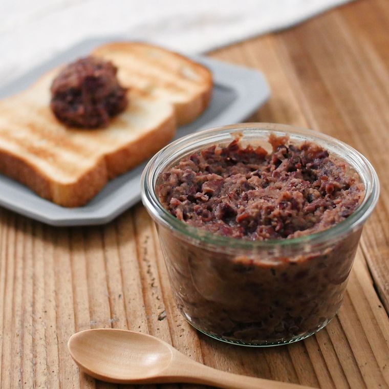 木の机の上に透明のガラスの容器に入ったつぶあんバターが置かれている