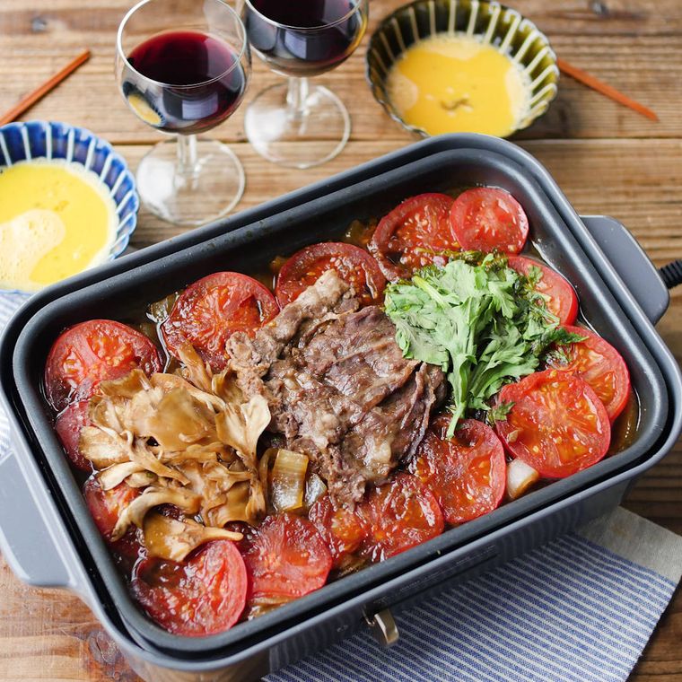 トマトすき焼きを作ったホットプレートに、溶き卵入りの取り皿と箸が添えられている様子