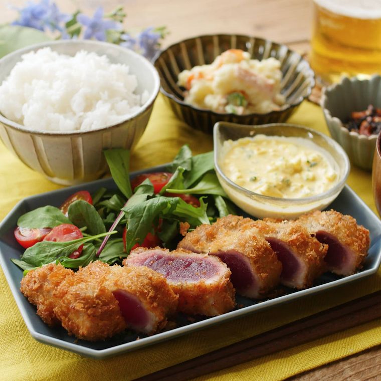 まぐろカツ、大葉タルタル入りの透明な器、サラダを盛り付けた紺色の八角皿に、ごはんとポテトサラダが添えられている様子