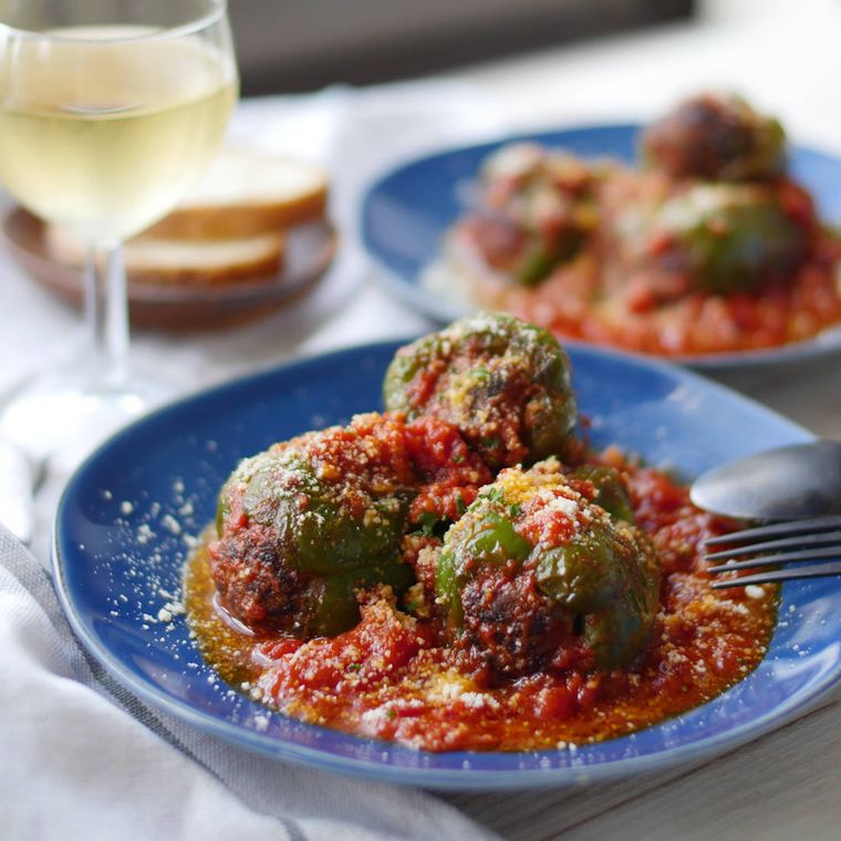 青い丸皿に盛られた丸ごとピーマンの肉詰めと、グラスに入った白ワイン