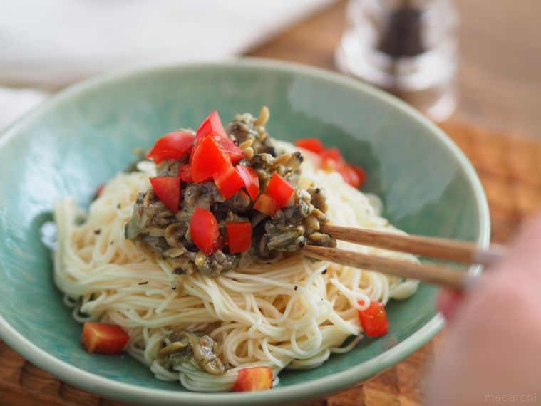 トマトと何にでも使えるあさりちゃんをのせたそうめんを箸でつまむ様子