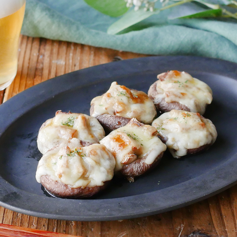 黒い皿に盛りつけられたしいたけのチーズ焼きとテーブルに置かれたビール