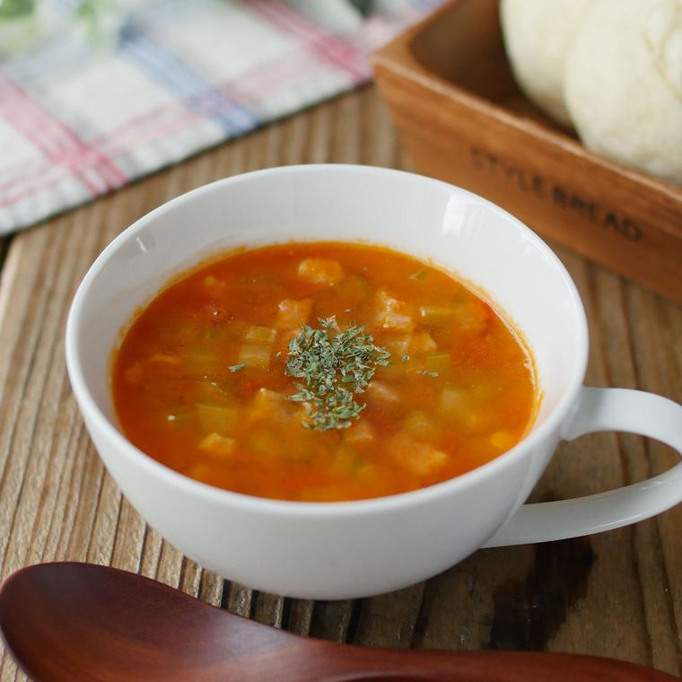 白い器にセロリとトマトのコンソメスープが入っていて手前に木のスプーンが置いてある