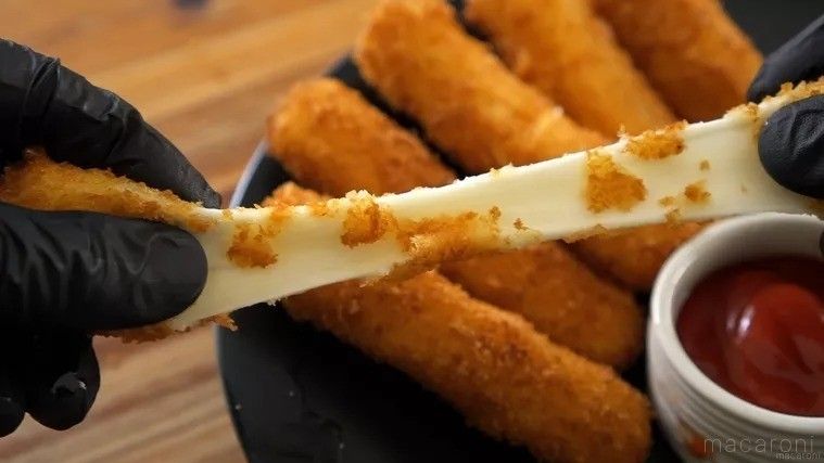 黒い手袋をした手でチーズスティックフライを引っ張ってのばしているところ