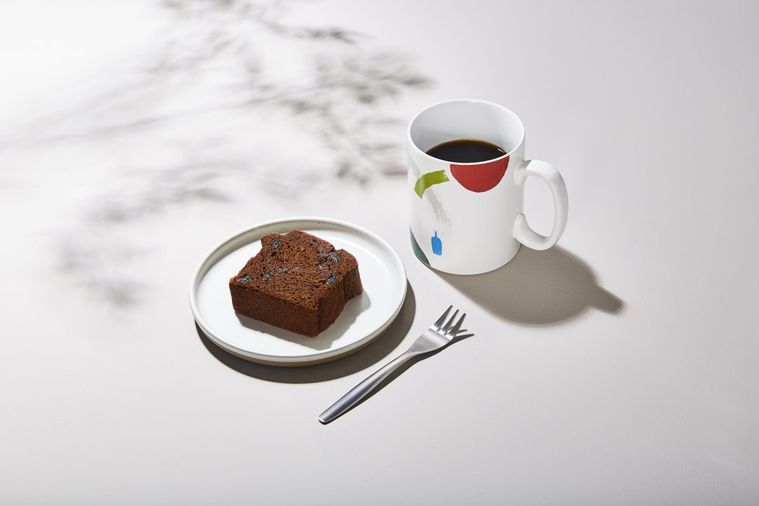 白いマグカップに入ったコーヒーと、カットされたチョコレートのパウンドケーキが白いおさらに乗ってテーブルに置かれている