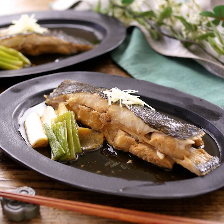 こげ茶色の皿に盛りつけられたかれい切り身と長ねぎの煮付け