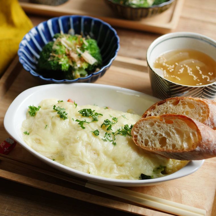 白いグラタン皿に盛られたブロッコリーと鮭の長芋グラタンと添えられたパン、スープとおひたし