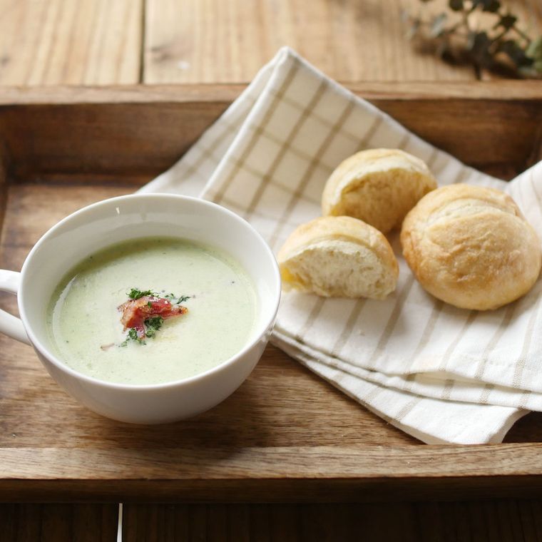 白いカップに盛り付けられた玉ねぎとズッキーニのポタージュにパンが添えられている